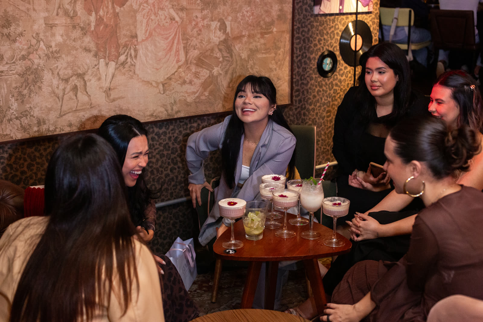 Grupo de mulheres rindo ao redor da mesa com drinks